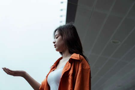Orange shirt girl standing at the awning of the shopping mall, release her hand out to check the rain.の写真素材