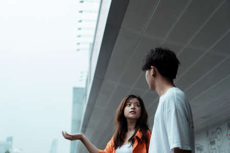 Teenage couple standing at the awning of the shopping mall, they look at each other and decide to stay until the rain stops.の写真素材