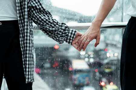 Close up shot of couple's hands that holding tightly with a rain on a glass as a background.の写真素材
