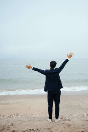 Black hair guy in dark suit standing on the beach spread his arms over his head like he welcome the wind of the sea.の写真素材