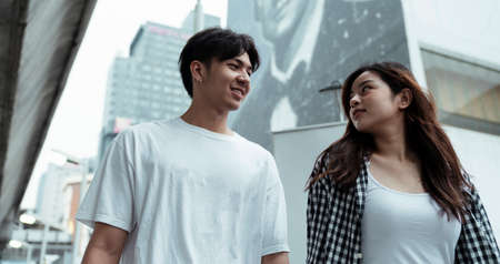 Low angle shot of teenage couple walk together in the city, look at each other.の写真素材