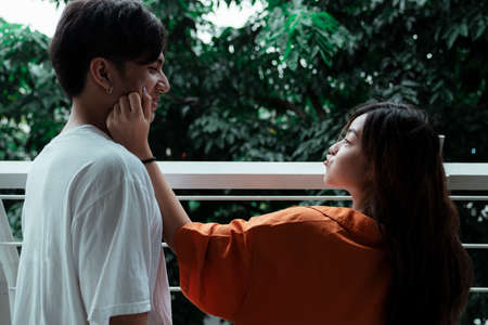 Orange shirt girl squeeze white t-shirt guy's cheek while she make a duck face.