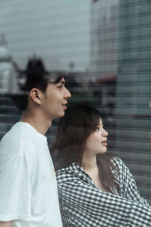 Teenage lover standing together behind the glass and look at interesting thing through the glass.の写真素材