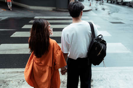 Back shot of teenage couple goint to walk across the road at zebra crossing together and hold each other hand.の写真素材