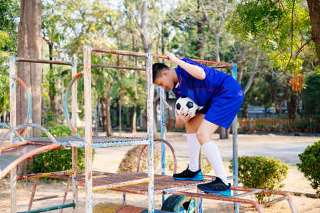 Boy in blue football suit play on the climb frame with ball.の写真素材