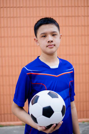 Football boy hold the ball in front of brown wall.の写真素材
