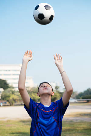 A boy in blue football suit throw the ball over his head. Throw the ball up into the air.