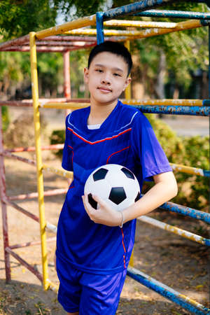 Young boy leaning against climb frame in the playground with football in his hand.の写真素材