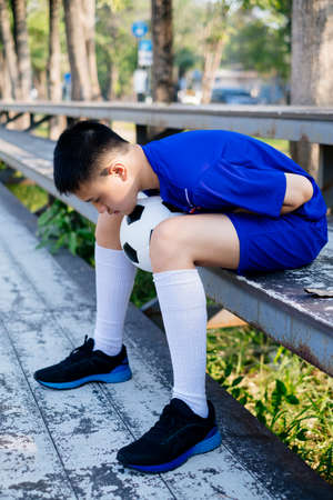 Young boy sitting on the stand with a ball between his legs and bend his body down.の写真素材
