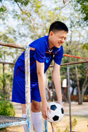 Happy boy in blue suit standing on the climb frame in the playground with football.の写真素材