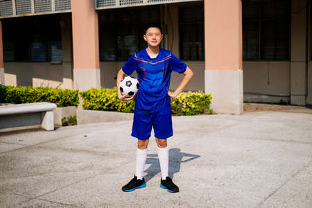 Prideful boy standing in front of the orange building with his football.