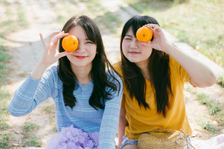 Two girls picnic in the park, raise the oranges at their eyes.の写真素材