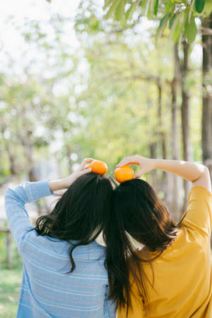 Two girls standing together and put the oranges on their head in the park.