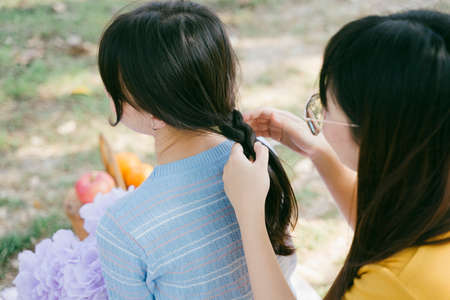 Yellow t-shirt girl do the hair design for blue t-shirt girl during picnic.の写真素材