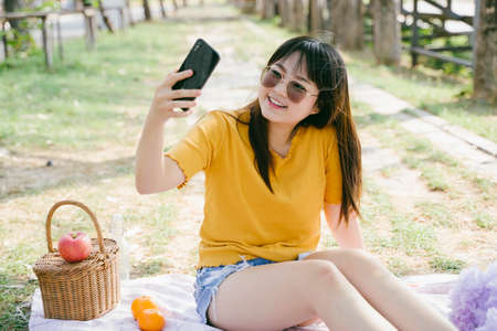 Yellow t-shirt woman take a selfie while sitting on the mat during picnic, wearing sunglasses.の写真素材