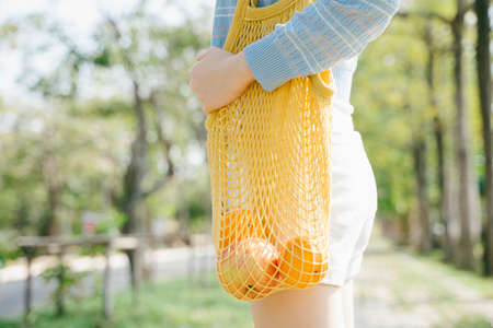 Cropped image of apple and orange in the net bag that the girl hold while standing in the park.