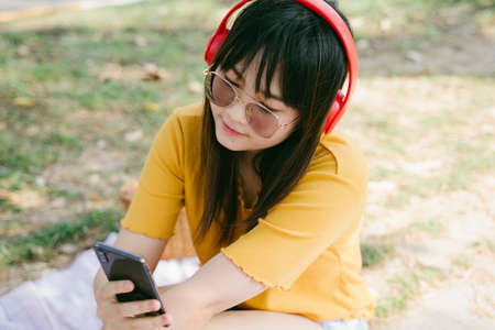 Yellow t-shirt girl wearing sunglasses and red headphone choose the music in smartphone application.の写真素材