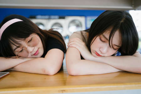Two girls prop their own head on their arms and sleep in the laundro mat.の写真素材