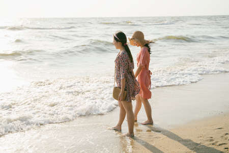 Two girls walking together on the beach look at the wave from the sea.の写真素材