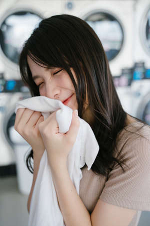 Cute girl hug the clean towel that she take out from the washing machine and smell it with smile.