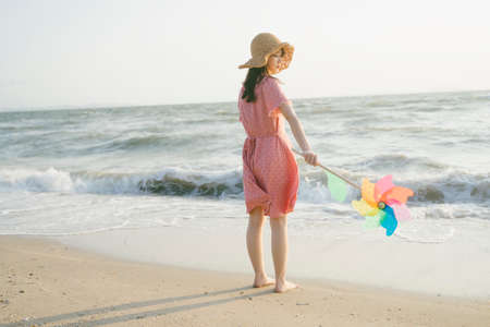Long hair girl standing on the beach with barefoot holding the colorful windmill with copy space.の写真素材