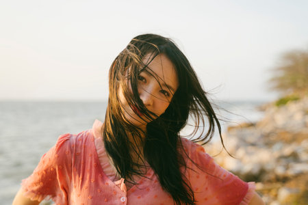 Cute girl with wet long hair smile to the camera while standing on the rock beach in windy evening.