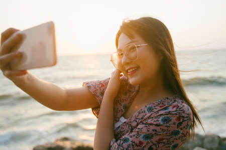 Long hair girl in sunglasses take a selfie with sunset in the evening at the sea.