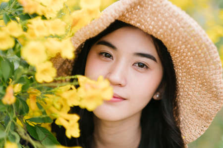Close up of Thai girl standing among yellow flowers looking at that flowers.の写真素材