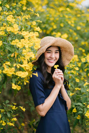 Smiling beauty girl wear brown hat hold yellow flower and standing among the flower on the tree.の写真素材