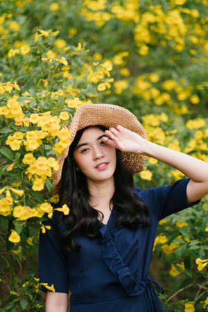 Portrait shot of curly long hair girl standing next to the yellow flower on the tree raise her hand cover her eye..の写真素材