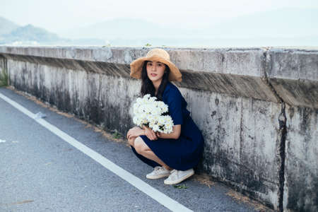 Blue dress girl sitting at the barricade with white flower, looking at the camera.