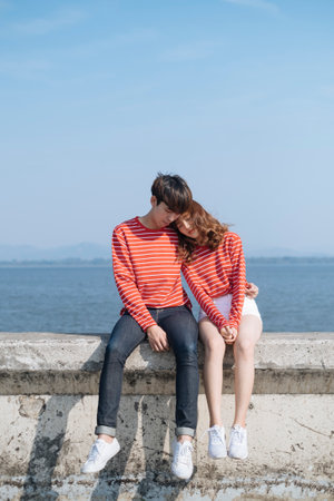 Teenage couple on the dam's barricade, a girl prop her head on her boyfriend's shoulder while the guy holding her waist.の写真素材