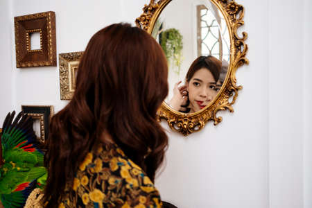 Cute curly long hair girl in yellow dress look at herself in the golden mirror.の写真素材