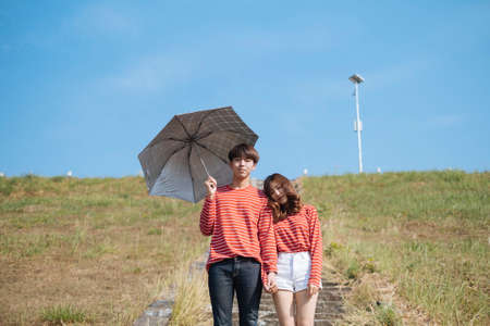 Curly long hair girl prop her head on her boyfriend's shoulder while he hold the umbrella under the blue sky, horizontal.の写真素材