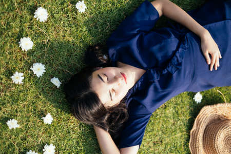 Beautiful woman in dark blue dress sleep on a hand in a field among the white flower.