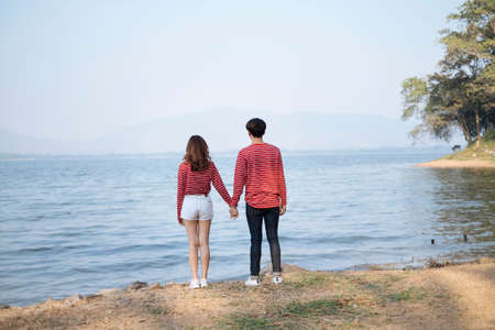 Teenage couple standing together at the lake and hold each other hand, looking far away.の写真素材