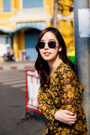 Cute curly long hair girl in yellow dress and sunglasses leaning at the pole next to the red barricade.の写真素材