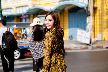 Back shot of cute curly long hair girl in yellow dress standing in the city.の写真素材