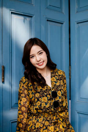 Cute curly long hair girl in yellow dress standing in front of blue folding door with sunlight and shadow.の写真素材