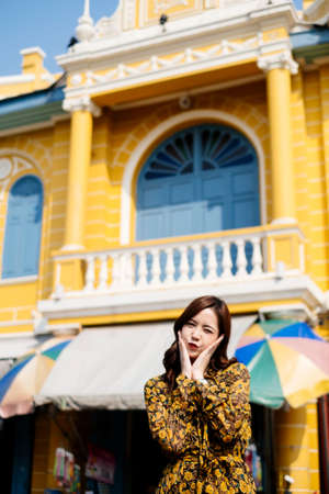 Curly long hair girl in yellow dress standing in front of blue and yellow building with cute act.