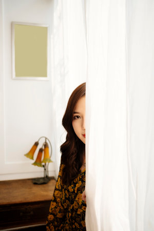 Cute curly long hair girl in yellow dress hiding back of white curtain.の写真素材