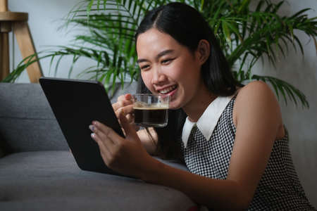 Asian women drink a morning coffee and use her tablet in the living room.