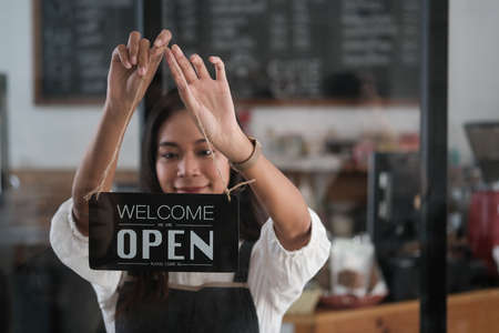 Asian women barista hanging sign on the door that show word Welcome and open.
