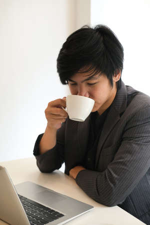Closed up view with business man drinking a coffee while looking on laptop computer in the office...