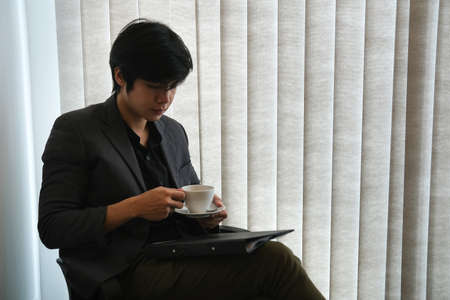 Portrait with a businessman sitting and hold a cup of coffee and document folder in office room.