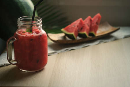Closed up with a jar of watermelon juice, watermelon and three pieces  slice of watermelon on the wooden desk with sunny light.の写真素材