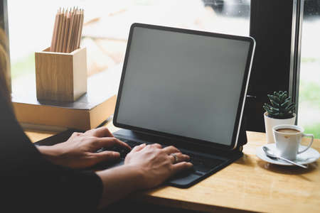 Closed up with female's hands typing on tablet with bright sunlight from outside the window.