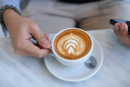 Top view with Asian male holding latte coffee and cellphone on mable table.