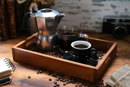 Mock up with Moka pot and cup of coffee shot in wooden tray decorated with coffee beans, camera and old book, wooden background, retro.の写真素材
