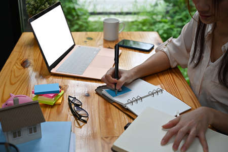 Closed up with office desk and businesswoman writing on notebook and empty screen of laptop place on wooden table.の写真素材